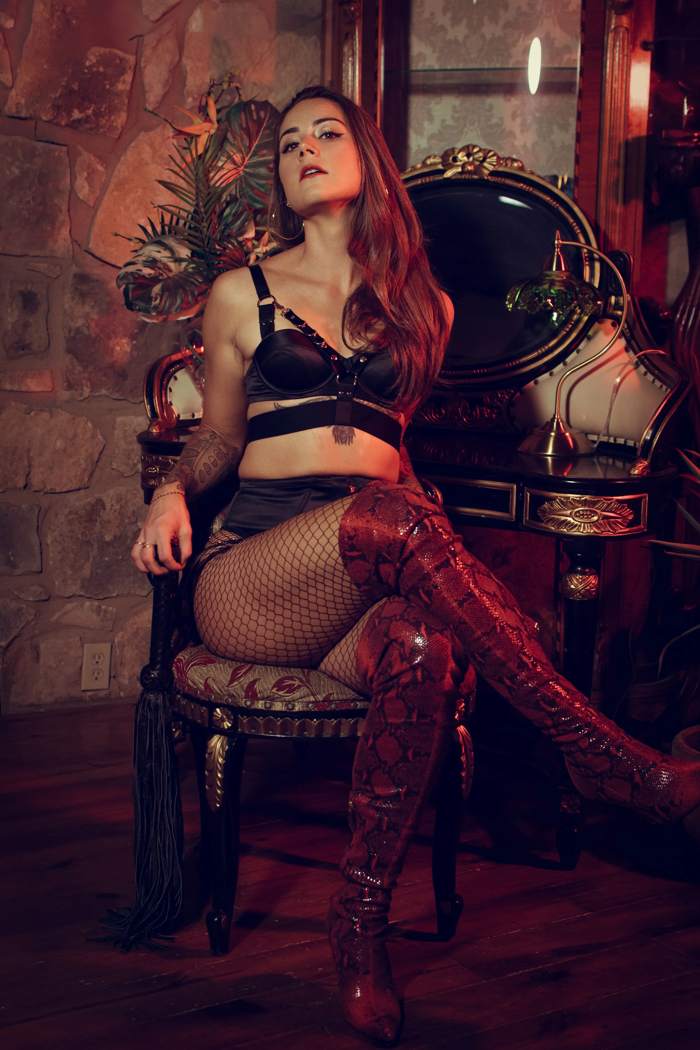 Mistress Athena Desire, Austin professional dominatrix, seated with a flogger in a vintage parlour